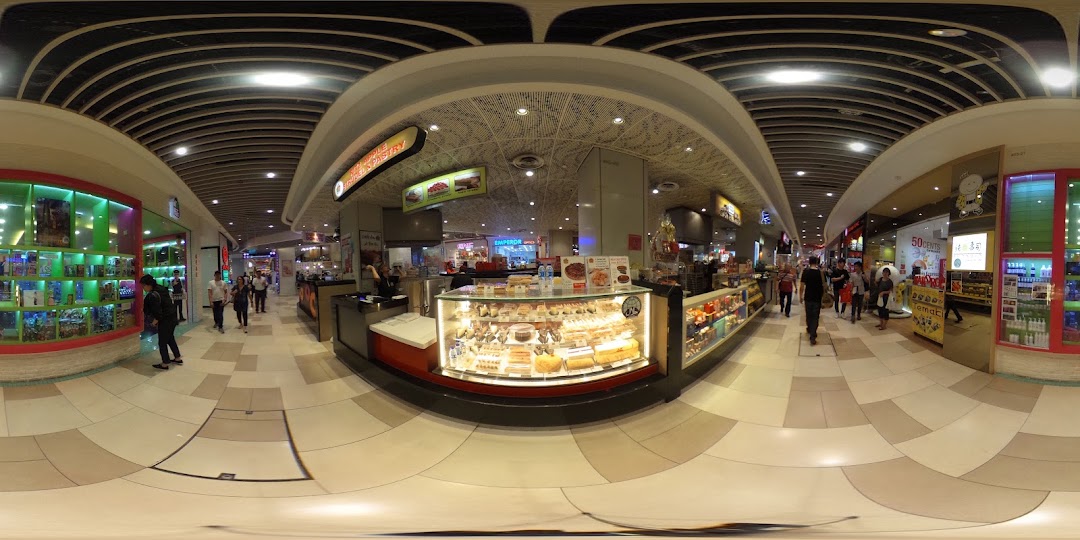 Interior view of a shopping mall with a pastry kiosk and people walking.