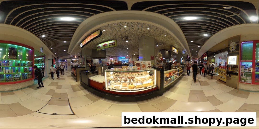 Interior view of a shopping mall with a pastry kiosk and people walking.