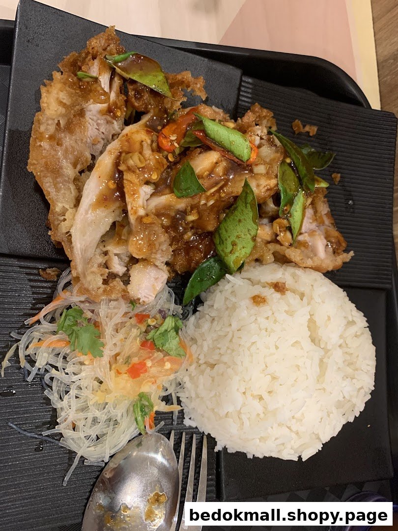 Fried chicken with rice and glass noodle salad on a black tray.