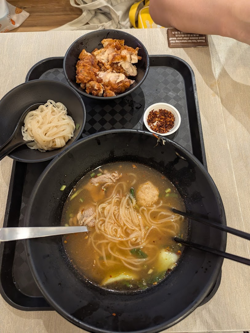 A tray with a bowl of noodles, fried chicken, and chili flakes.