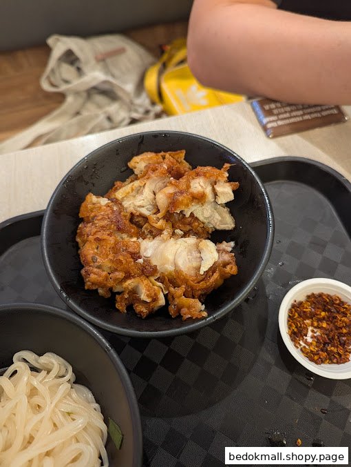 Fried chicken, noodles, and chili flakes on a black tray.