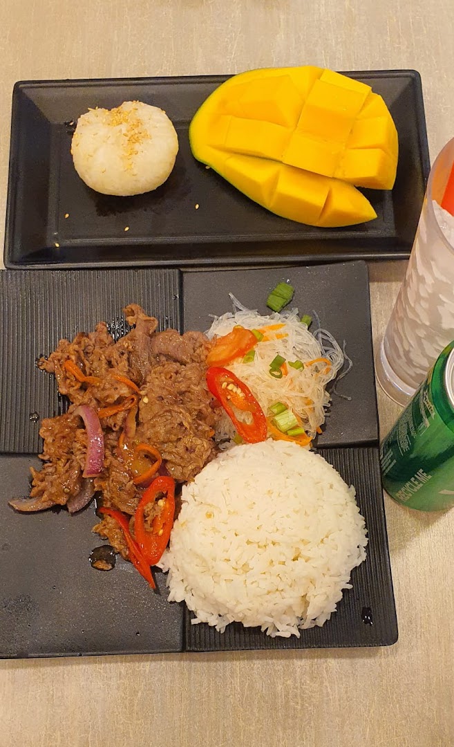 Plates of beef, rice, noodles, mango sticky rice, and a drink on a table.