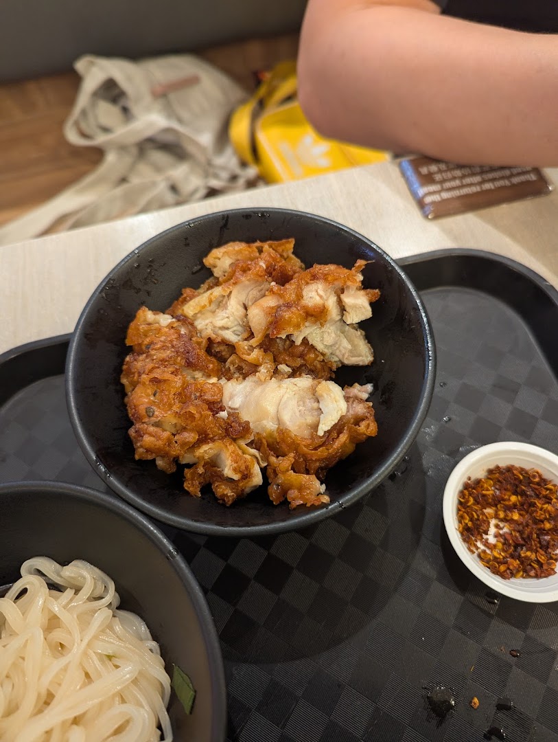 A bowl of fried chicken, noodles, and chili flakes on a black tray.