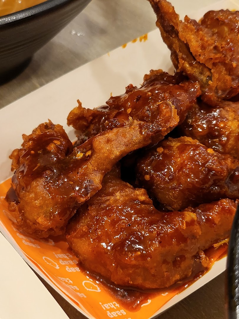 Close-up of saucy fried chicken wings in a white container.