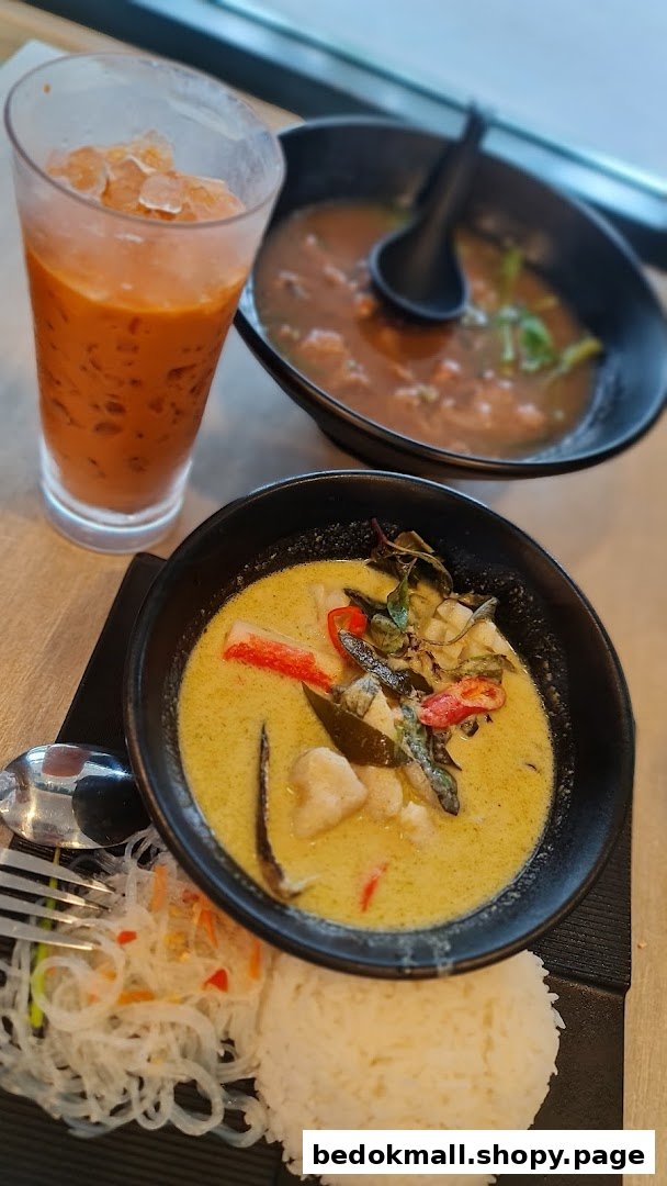 Thai green curry, rice, soup, and iced tea on a table.