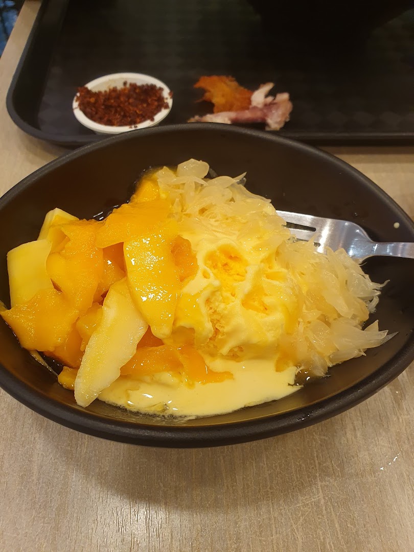 A bowl of mango and pomelo dessert with a fork on a table.