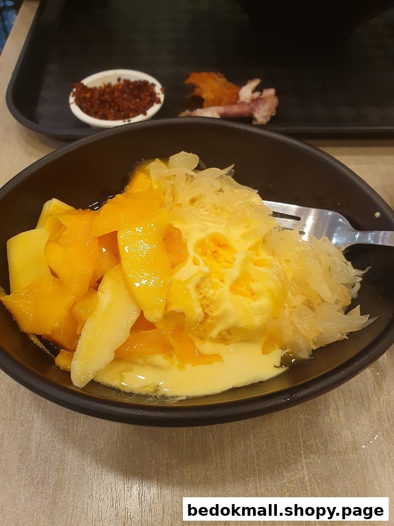 A bowl of mango and pomelo dessert with a fork on a table.