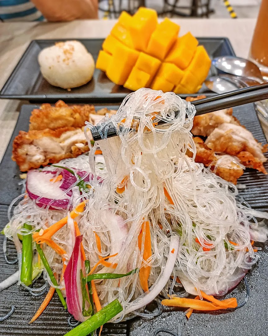 Chopsticks picking up glass noodles, with fried chicken and mango on plates.
