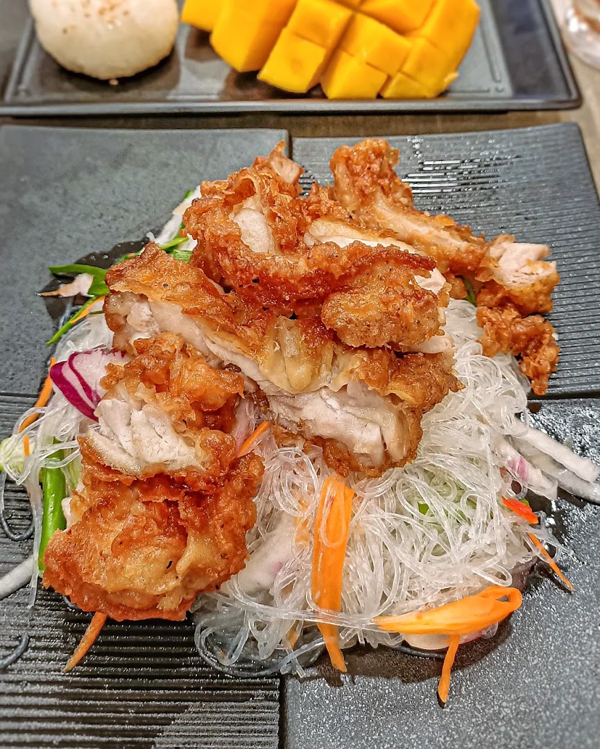 A dish of fried chicken with clear noodles and mango in the background.