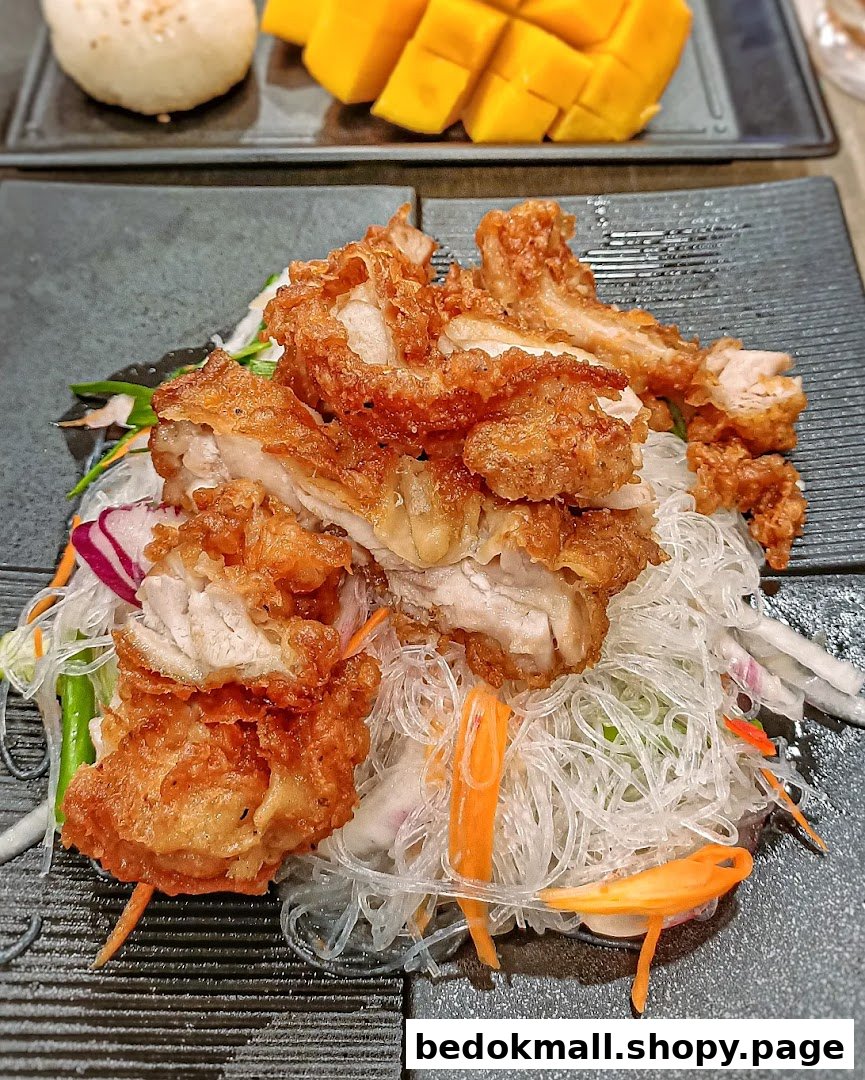 A dish of fried chicken with clear noodles and mango in the background.