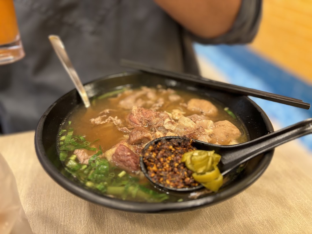 Close-up of a bowl of beef noodle soup with chili flakes on a spoon.