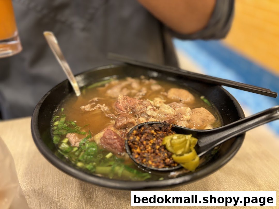 Close-up of a bowl of beef noodle soup with chili flakes on a spoon.