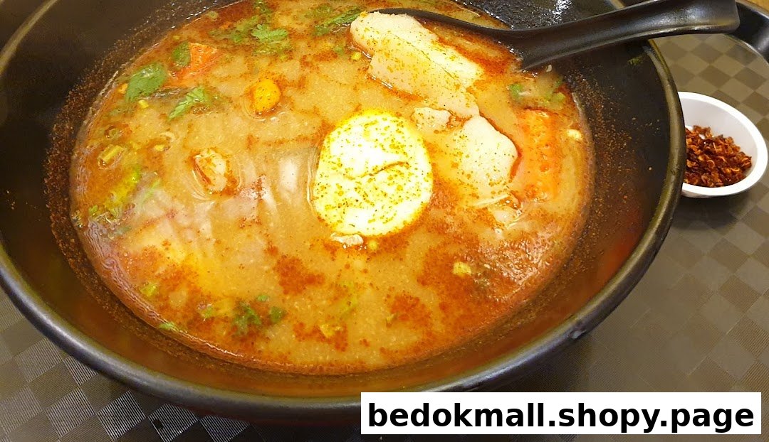 A bowl of Thai soup with egg, vegetables, and a side of chili flakes.