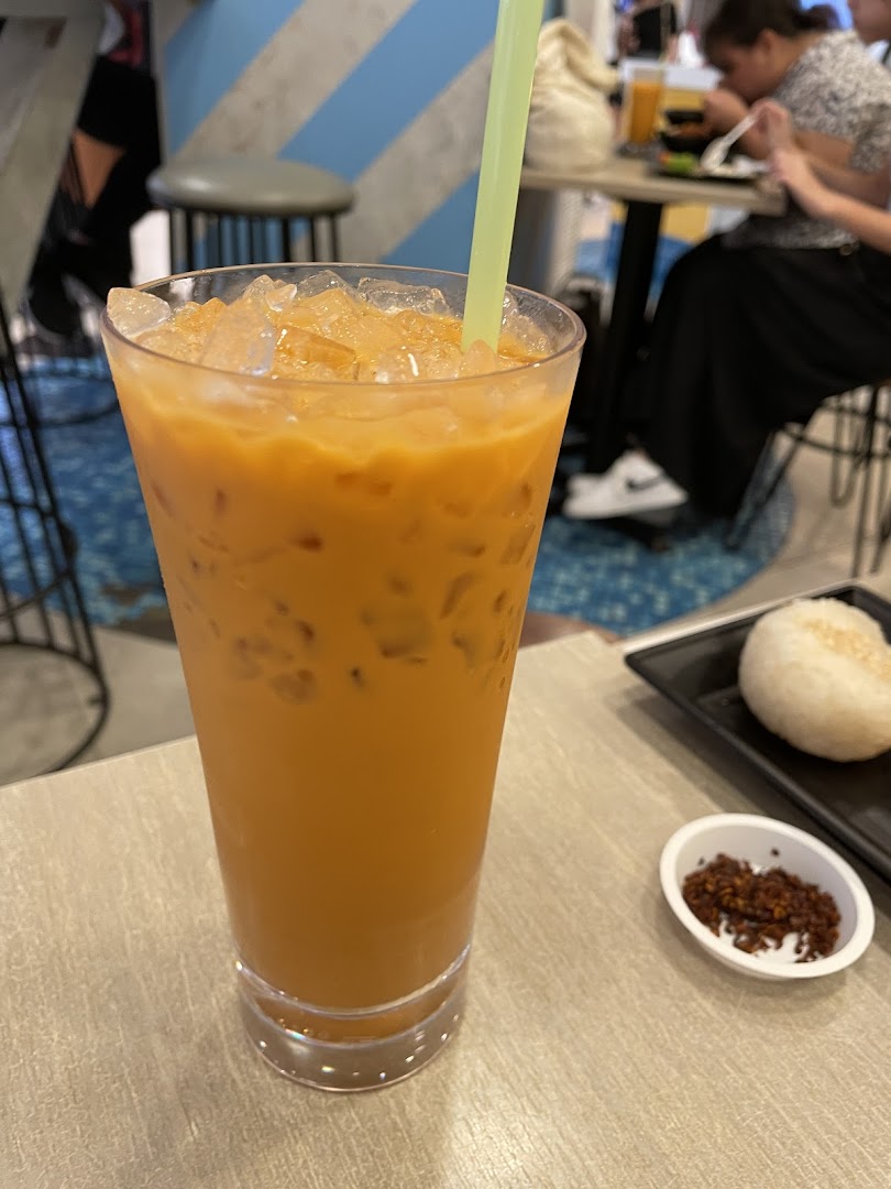 A tall glass of iced tea with a straw on a table, with food nearby.