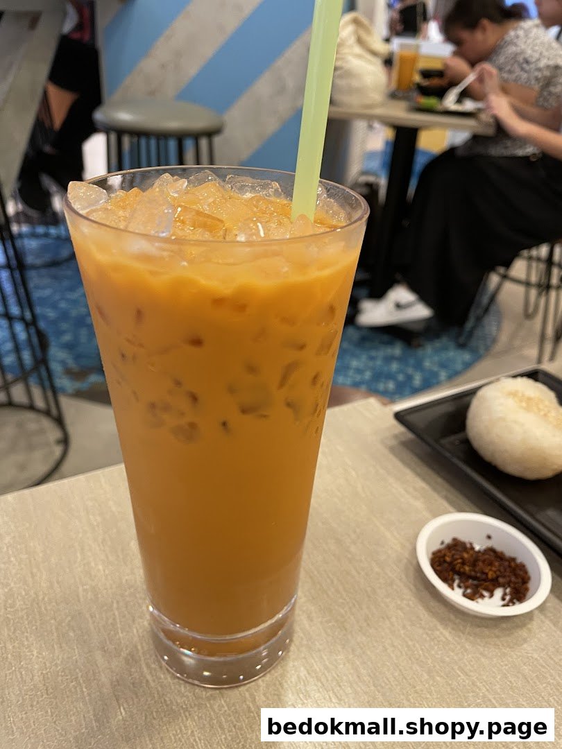 A tall glass of iced tea with a straw on a table, with food nearby.