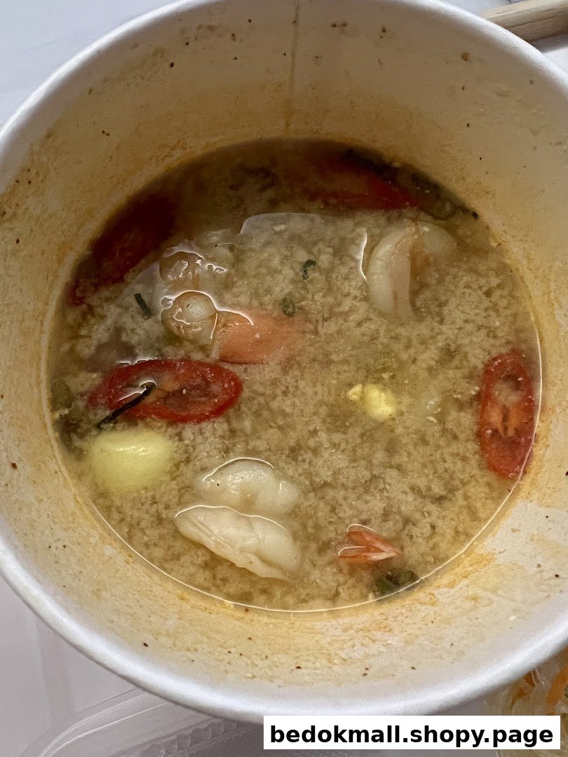 Bowl of Thai soup with shrimp, tomatoes, and other ingredients.