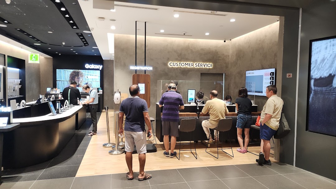 Interior view of a Samsung store with customers at product displays and service counters.