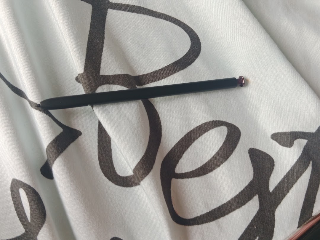 A black stylus with a purple tip rests on white patterned fabric.
