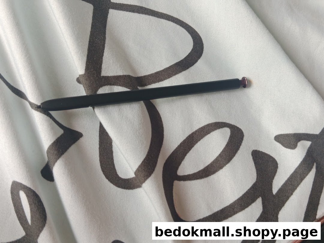 A black stylus with a purple tip rests on white patterned fabric.