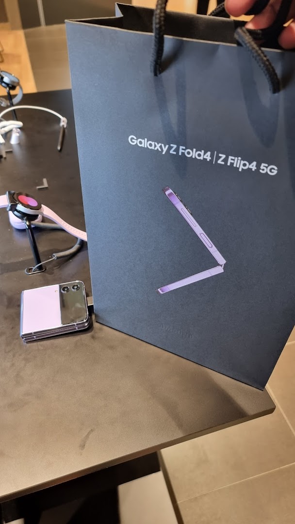 Samsung shopping bag, Z Flip phone, and smartwatch on a display table.