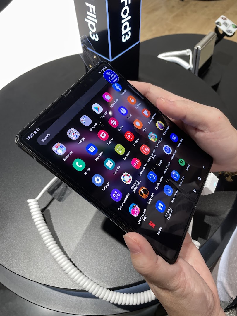 Person holding a Samsung foldable phone displaying app icons in a retail store.