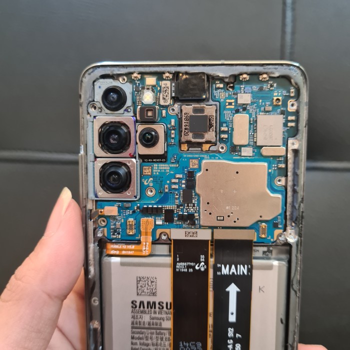 A hand holds a disassembled smartphone, revealing its internal circuit board, cameras, and battery.