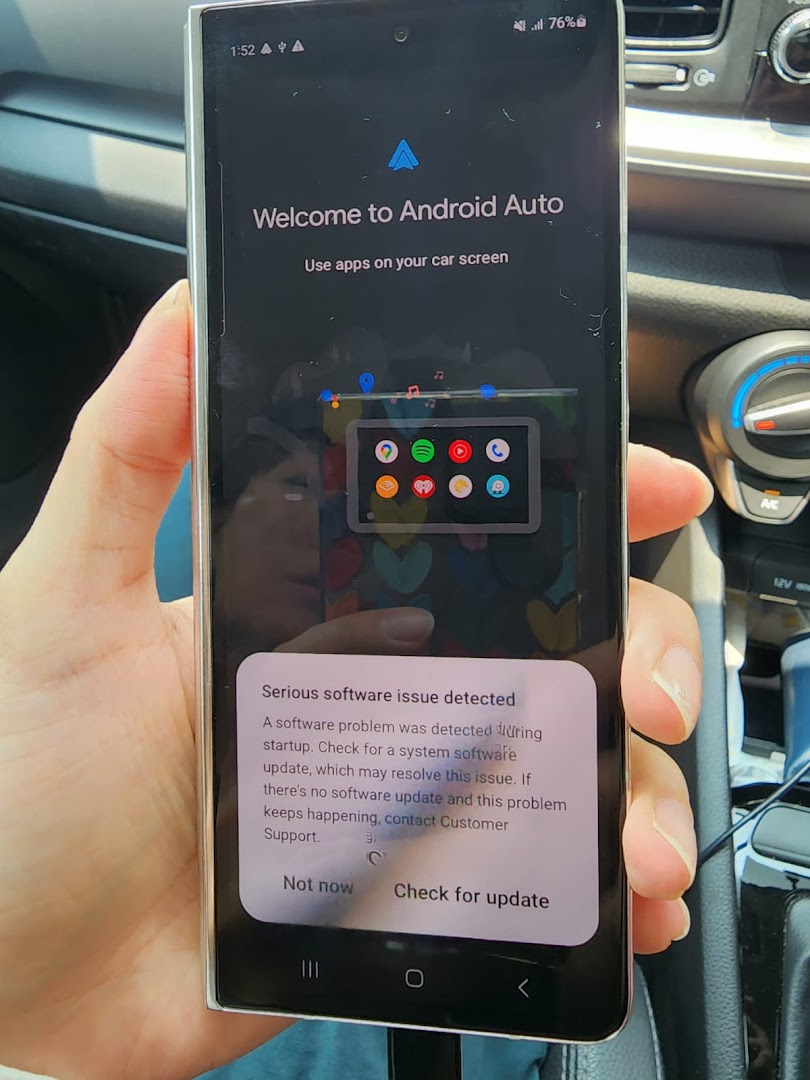 Hand holding a smartphone displaying an Android Auto screen and software error in a car.