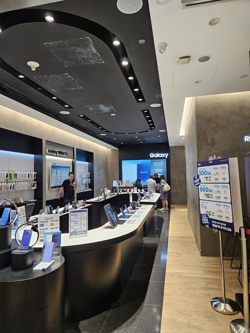 Interior of a Samsung store with display tables, electronic devices, and customers.