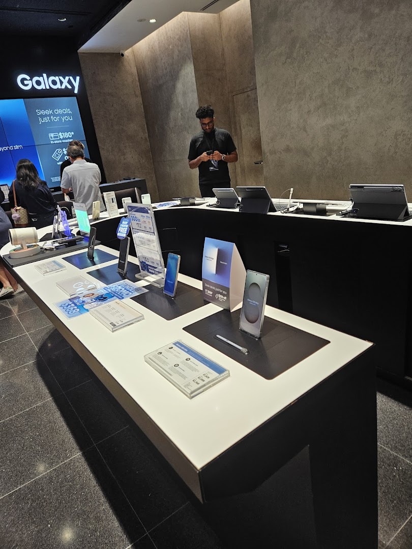 Interior of a Samsung store showing display tables with products and people.