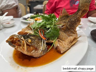 A whole fried fish dish with sauce and garnish on a white plate.