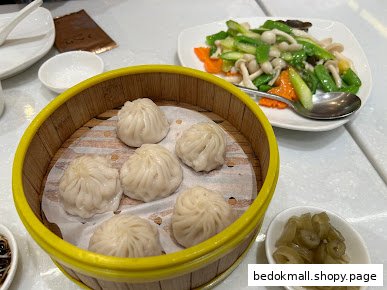 Steamed dumplings in a bamboo basket with a side of stir-fried vegetables.