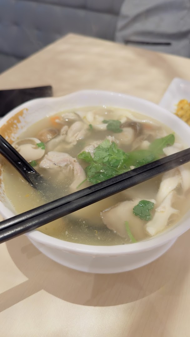 A steaming bowl of soup with meat, mushrooms, and herbs on a table.