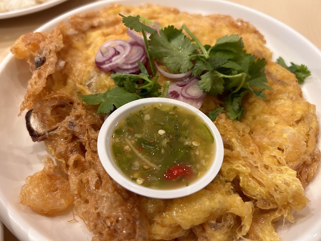 Close-up of a fried omelet dish with herbs, red onions, and dipping sauce.