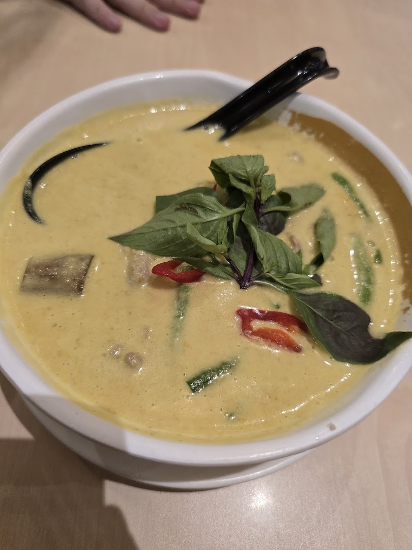 A bowl of yellow curry or soup with basil, chili, and a spoon.