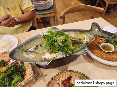 A table with a large steamed fish dish and other Thai food.