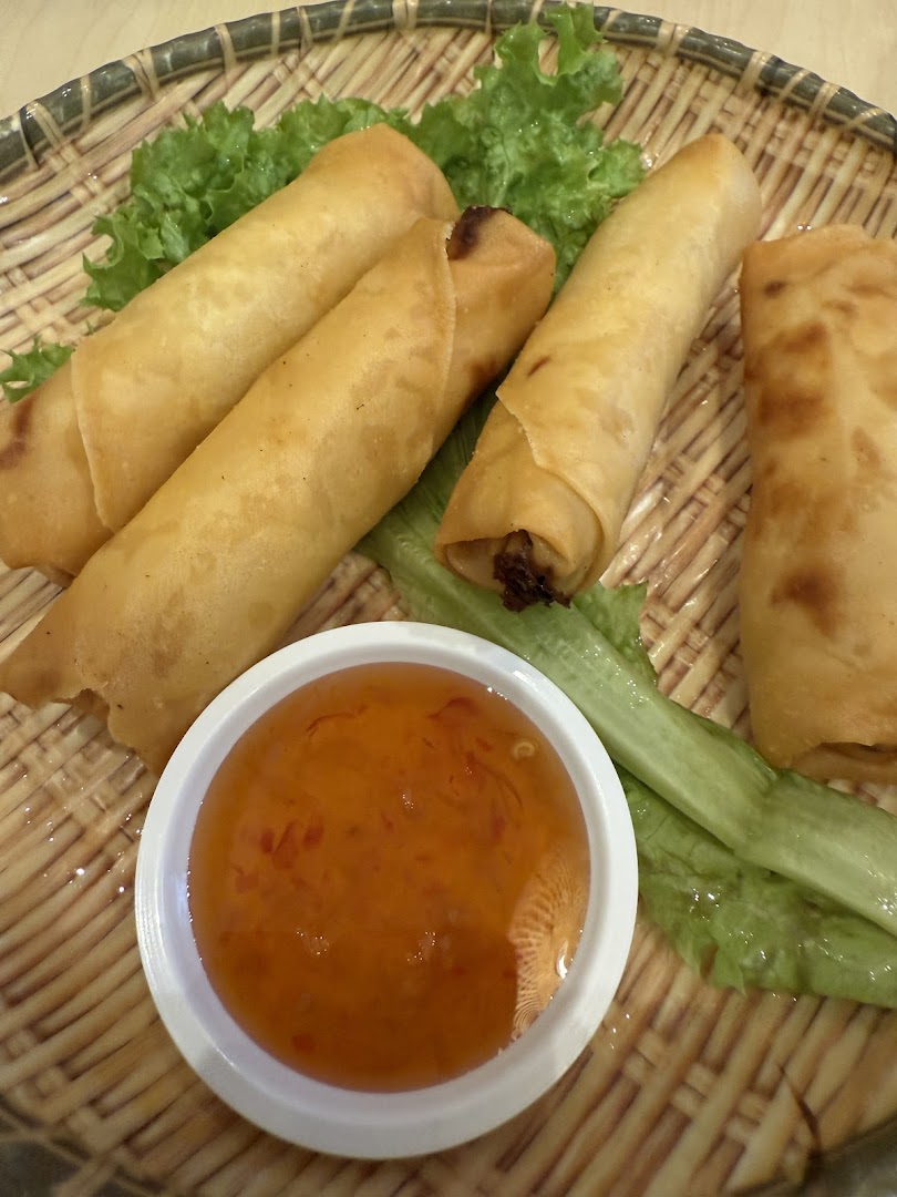 Fried spring rolls with dipping sauce and lettuce on a woven plate.