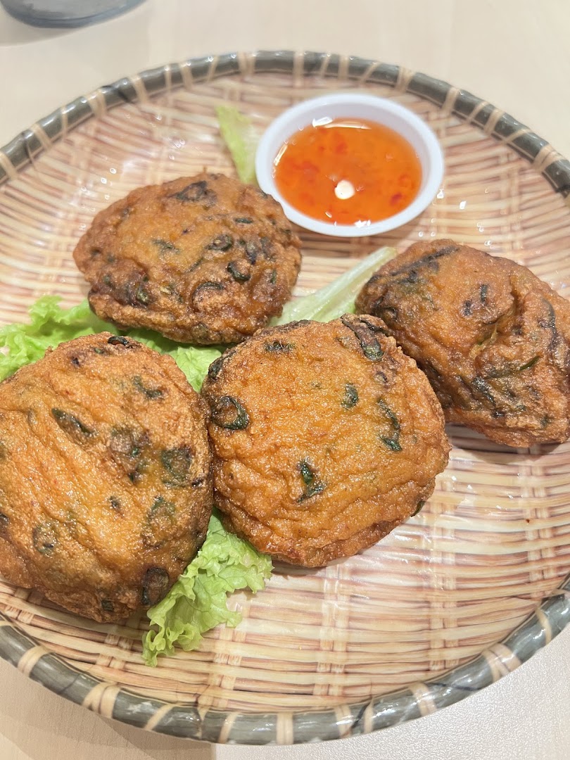 Four fried patties with dipping sauce on a woven plate.