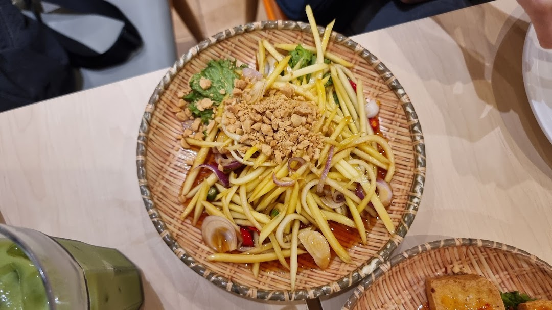 A close-up of a mango salad with peanuts in a woven basket on a table.