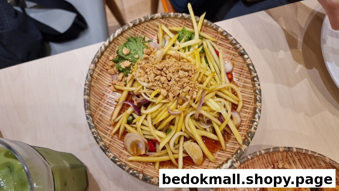 A close-up of a mango salad with peanuts in a woven basket on a table.