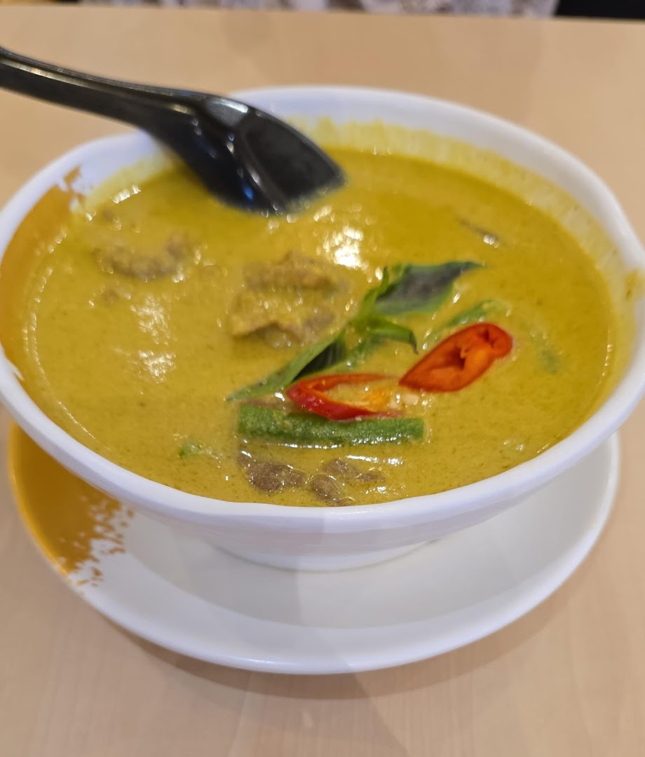 A bowl of green curry with meat, chili, and basil.