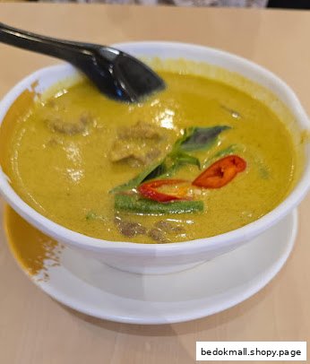 A bowl of green curry with meat, vegetables, and a spoon.