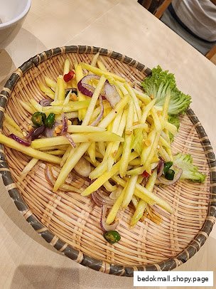 Mango salad with red onions and chilies served on a woven tray.