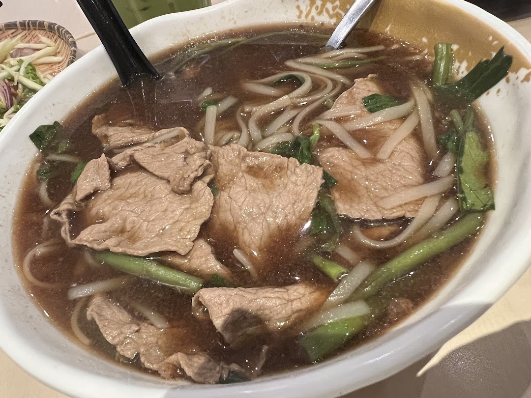 A close-up of a bowl of beef noodle soup with vegetables.