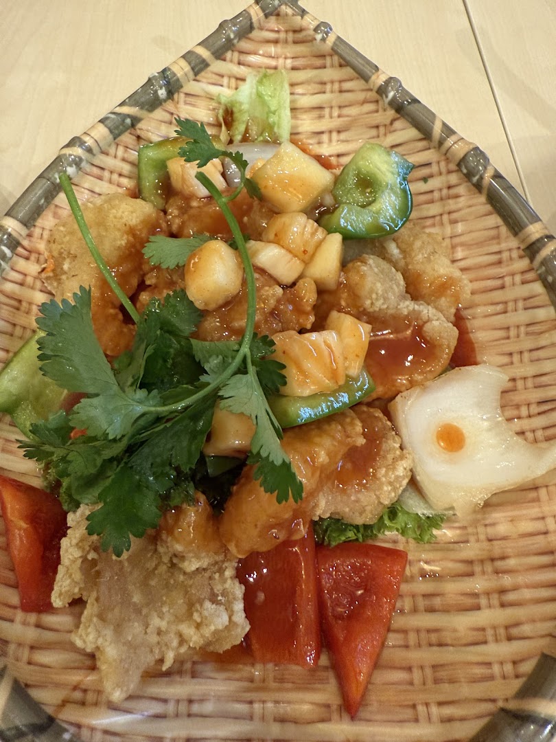 A sweet and sour dish with fried items and vegetables on a woven plate.