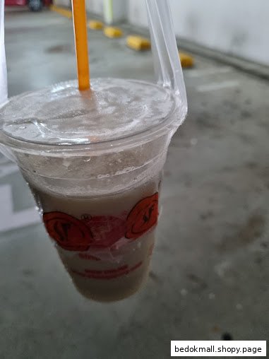 A plastic cup with a drink, straw, and carrier in a parking area.