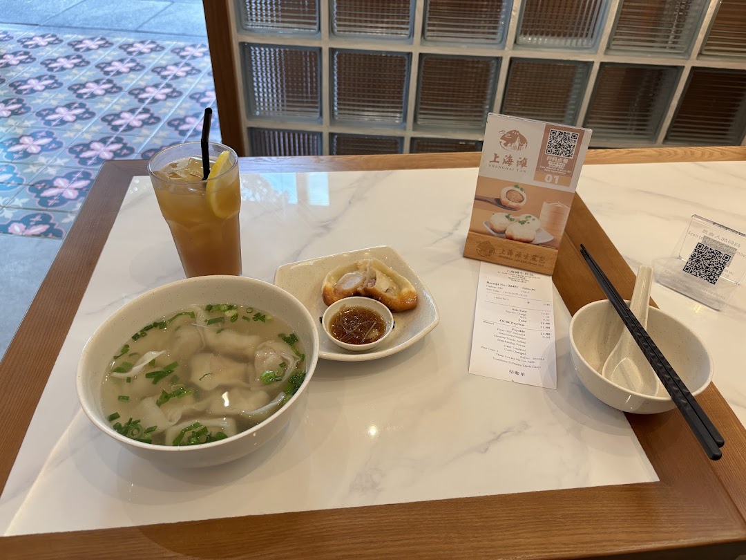 A table with a bowl of soup, pan-fried buns, and a drink.