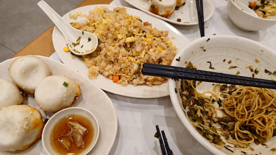 Plates of fried rice, pan-fried buns, and noodles on a table.