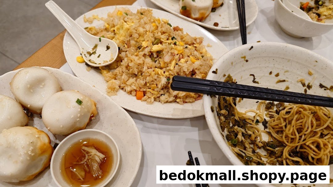 Plates of fried rice, pan-fried buns, and noodles on a table.