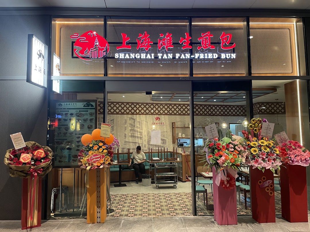 Shop front with large sign, glass entrance, and celebratory flower arrangements.