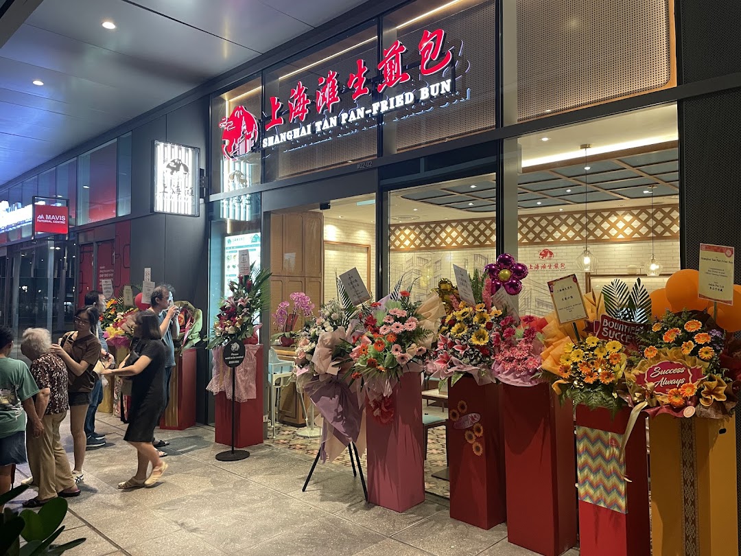 Exterior of Shanghai Tan Pan-Fried Bun shop with flower arrangements and people.